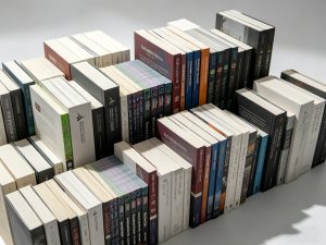 A large display of custom printed softcover books stacked together, showcasing professional perfect binding with clean, flat spines in varied thicknesses